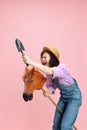 Comic portrait of cheerful young girl, gardener in denim overalls and hat having fun isolated on pink background Royalty Free Stock Photo