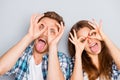 Comic portrait of funny lovers showing tongues and holding fingers near eyes like glasses