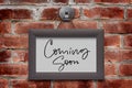 Coming soon. Handwritten inscription in a wooden frame. Brown brick wall