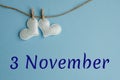 Commemorative date November 3 on a blue background with white hearts with clothespins, flat lay. Holiday calendar concept