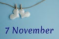 Commemorative date November 7 on a blue background with white hearts with clothespins, flat lay. Holiday calendar concept