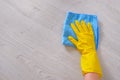 Commercial cleaning company concept. Hand in rubber protective glove with blue microfiber cloth is wiping wooden floor. Copy space Royalty Free Stock Photo