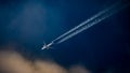 Commercial passenger aircraft flying over a blue sky, leaving a trail of contrails