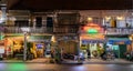 Commercial street at night. Shops, Chinese style houses, restaurant terraces, people. Two story houses. Awnings with Vietnamese