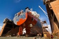 Commercial vessel undergoes maintenance in floating dock. Workers paint, repair hull, under clear skies at shipyard Royalty Free Stock Photo