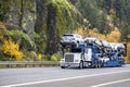 Commercial white big rig car hauler semi truck transporting cars on modular two level semi trailer driving on the autumn highway Royalty Free Stock Photo