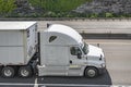 Commercial white big rig long hauler semi truck transporting cargo in dry van semi trailer driving on the divided highway road at Royalty Free Stock Photo