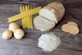 Bad carbohydrates to avoid such as white bread, pasta, rice, potatoes and buscuits laying on top of a wooden table