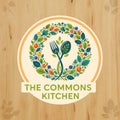 The Commons Kitchen logo featuring a fork and spoon with a leafy design on a wooden background Royalty Free Stock Photo