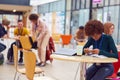 Communal Area Of Busy College Campus With Female Student Working At Tables And Using Mobile Phone