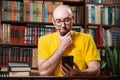 Communication. A bald smiling man with glasses uses a smartphone. In the background is a library and shelves of books. Concept of