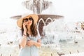 Communication. Beautiful young woman in a hat and glasses, smiling and calling on the phone. There`s a fountain in the background