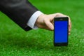 Communication and Business Subject: Hand in a black suit holding a modern phone with blue screen in the background of green grass Royalty Free Stock Photo