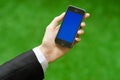 Communication and Business Subject: Hand in a black suit holding a modern phone with blue screen in the background of green grass Royalty Free Stock Photo