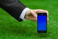 Communication and Business Subject: Hand in a black suit holding a modern phone with blue screen in the background of green grass Royalty Free Stock Photo