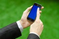 Communication and Business Subject: Hand in a black suit holding a modern phone with blue screen in the background of green grass Royalty Free Stock Photo