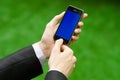 Communication and Business Subject: Hand in a black suit holding a modern phone with blue screen in the background of green grass Royalty Free Stock Photo