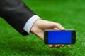 Communication and Business Subject: Hand in a black suit holding a modern phone with blue screen in the background of green grass Royalty Free Stock Photo
