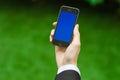 Communication and Business Subject: Hand in a black suit holding a modern phone with blue screen in the background of green grass Royalty Free Stock Photo