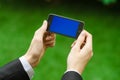 Communication and Business Subject: Hand in a black suit holding a modern phone with blue screen in the background of green grass Royalty Free Stock Photo