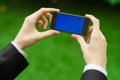 Communication and Business Subject: Hand in a black suit holding a modern phone with blue screen in the background of green grass Royalty Free Stock Photo