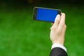 Communication and Business Subject: Hand in a black suit holding a modern phone with blue screen in the background of green grass Royalty Free Stock Photo