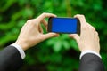 Communication and Business Subject: Hand in a black suit holding a modern phone with blue screen in the background of green grass Royalty Free Stock Photo