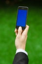 Communication and Business Subject: Hand in a black suit holding a modern phone with blue screen in the background of green grass Royalty Free Stock Photo