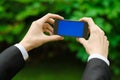 Communication and Business Subject: Hand in a black suit holding a modern phone with blue screen in the background of green grass Royalty Free Stock Photo