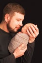 Communication father and son. Holiday concept Father`s Day. Father with a beard holds a newborn in his arms on a black background