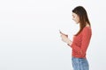 Communication is fun. Profile shot of satisfied charming happy woman in striped blouse, holding smartphone, typing