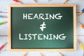 Hearing not equal listening written on chalkboard with coloured pencils on wooden Royalty Free Stock Photo