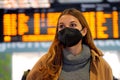 Commuter woman wearing KN95 FFP2 face mask at the airport to protect from virus. Young caucasian woman with timetables information