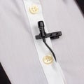 A compact black lav mic is secured on a white buttoned shirt, capturing the setup for professional audio recording Royalty Free Stock Photo