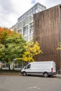 Compact cargo mini van delivered goods to client at multi-apartment high-rise building with wood wall and standing on the autumn