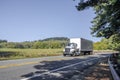 Compact day cab big rig semi truck transporting local cargo in dry van semi trailer driving on the winding narrow road with forest Royalty Free Stock Photo