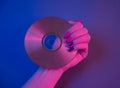 Compact disc in purple neon light and female hand with retrowave manicure.
