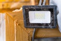 A compact LED spotlight hangs on a dismantled plastic window close-up. Economical lighting on construction sites