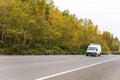 Compact mini van with leaders on the roof driving on autumn road with yellow trees