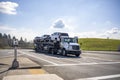 Compact white big rig car hauler semi truck transporting cars on the two level module semi trailer standing on the crossroad