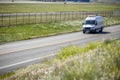 Compact white cargo mini van with refrigerator unit on the roof driving on the local road with field flowers Royalty Free Stock Photo