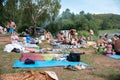 Companies of people rest closely on the bedspreads on the wooded shore of the lake on a summer day