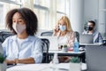 Company employees work in office. Multiracial managers in protective masks at workplaces with antiseptics and laptops Royalty Free Stock Photo