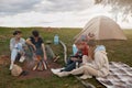 Company of friends hikers resting at fire at camp site and talking with hot drinks. Camping.