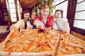 The company of guys in the pizzeria. Four friends in a cafe on the background of a large pizza on a wooden board.