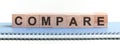 COMPARE - a word made of wooden blocks with black letters, a row of blocks is located on a blue Notepad Royalty Free Stock Photo