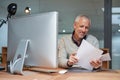 Comparing his paper and digital workflow. Portrait of a smiling mature businessman reading paperwork while sitting at Royalty Free Stock Photo