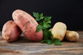 Comparison of sweet potatoes batata and ordinary potatoes on rustic wooden table with black background. Decorated with parsley Royalty Free Stock Photo