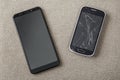 Comparison of two black mobile phones, old cellphone with cracked screen and new modern on light cloth copy space background. Royalty Free Stock Photo