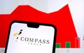 Compass Group logo on a smartphone screen and it`s real share price chart with a sharp drop seen on the blurred background